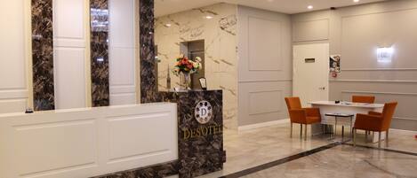 Un hall d’hôtel avec un comptoir de réception en marbre, un vase de fleurs et un coin repas comprenant des chaises et une table.