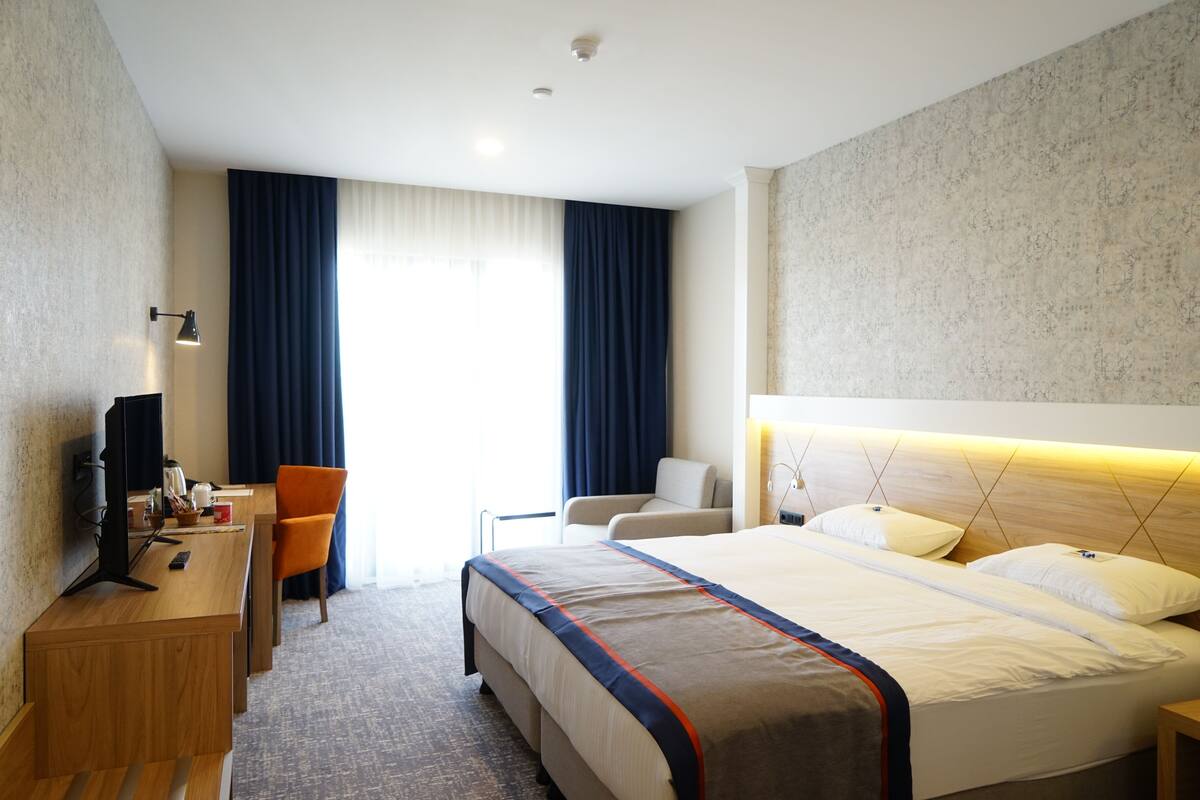 A hotel room with a bed, a desk with a computer, a chair, and a television.