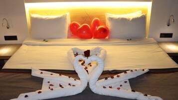 Habitación de hotel con cama, almohadas y una original disposición de toallas en forma de cisnes adornados con pétalos de rosa.