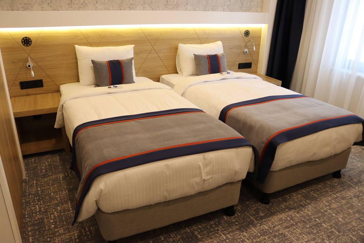 A hotel room with two beds, each with a headboard, bedside tables, and a carpeted floor.