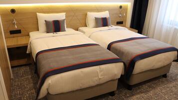A hotel room with two beds, each with a headboard, bedside tables, and a carpeted floor.