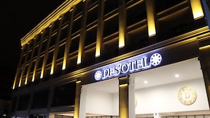 Fachada de un hotel iluminada de noche, con la señalización que dice "DESOTEL".