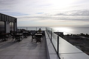 A terrace with tables and chairs overlooking the sea.
