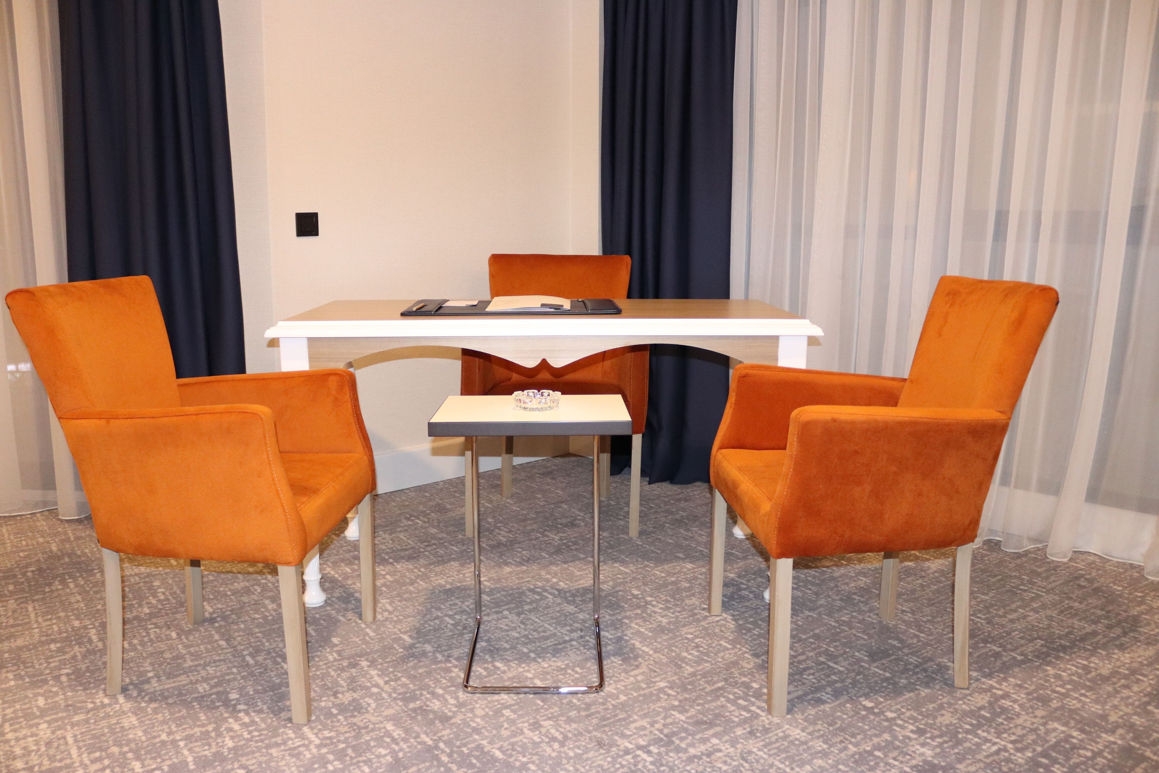 Un salón de conferencias con una mesa blanca, cuatro sillas anaranjadas y una mesita auxiliar.