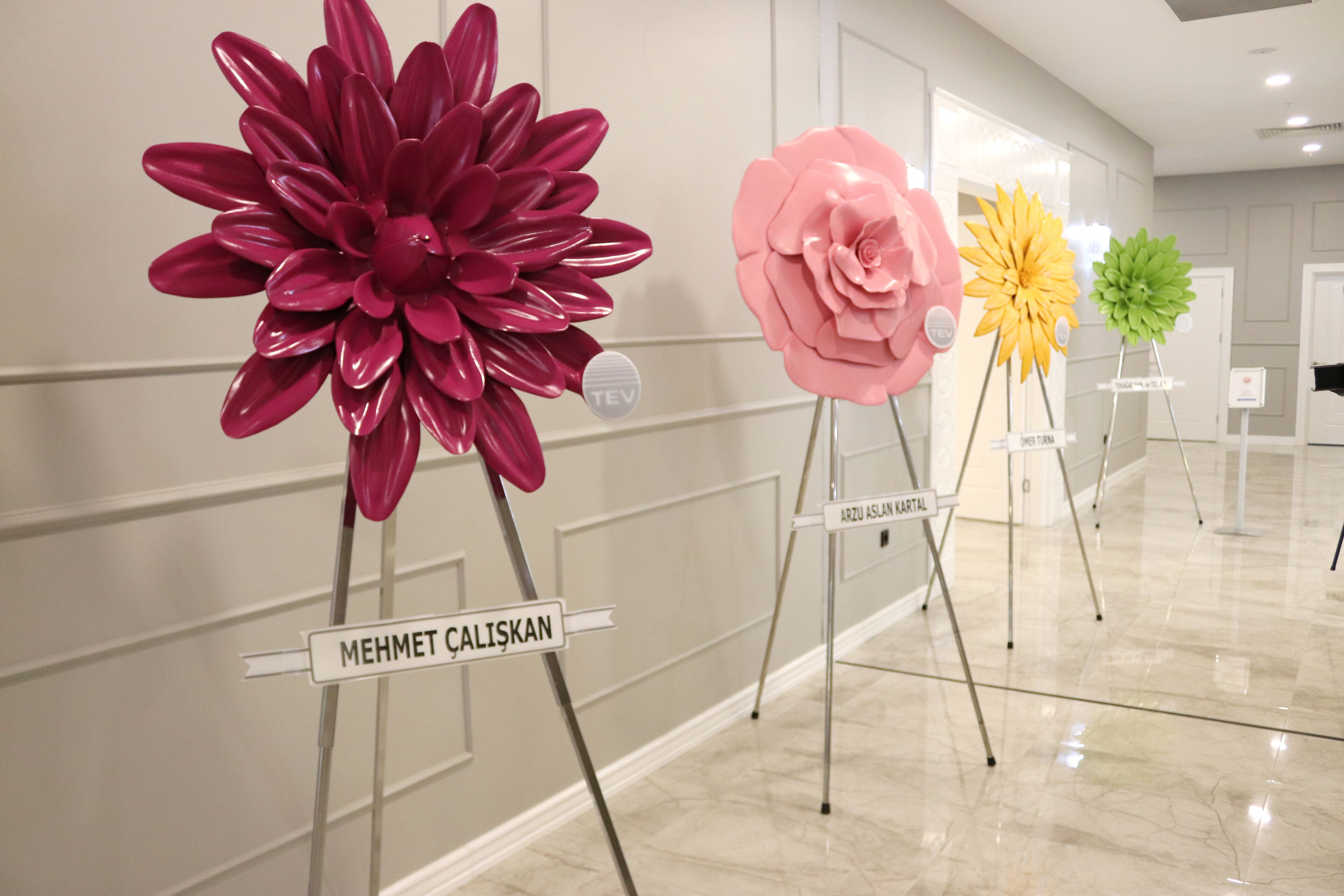 A hallway with three large floral sculptures on pedestals, each labeled with a name.