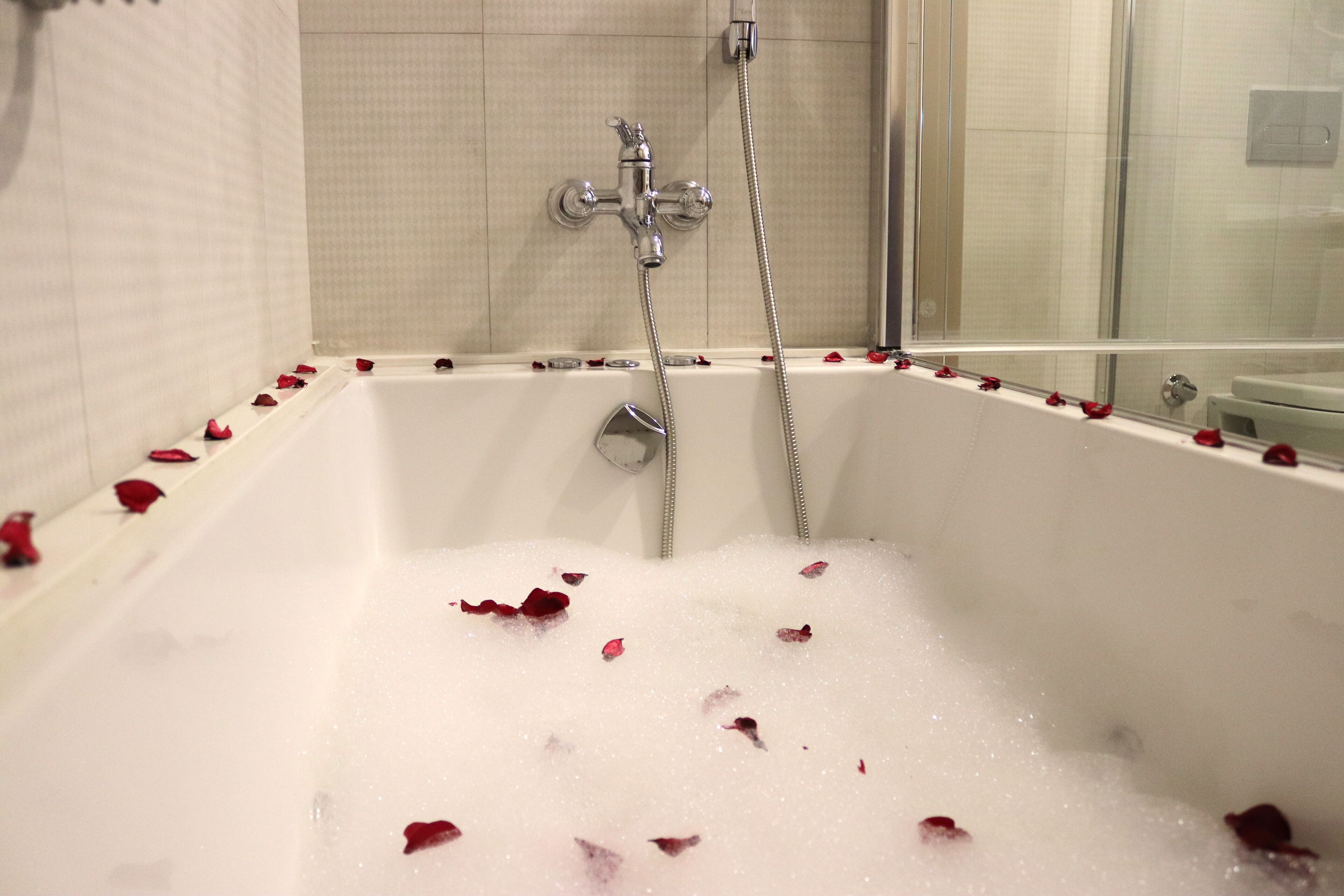 Une baignoire parsemée de pétales de rose, une pomme de douche et une paroi de douche en verre.