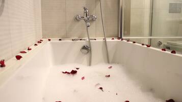 Une baignoire parsemée de pétales de rose, une pomme de douche et une paroi de douche en verre.