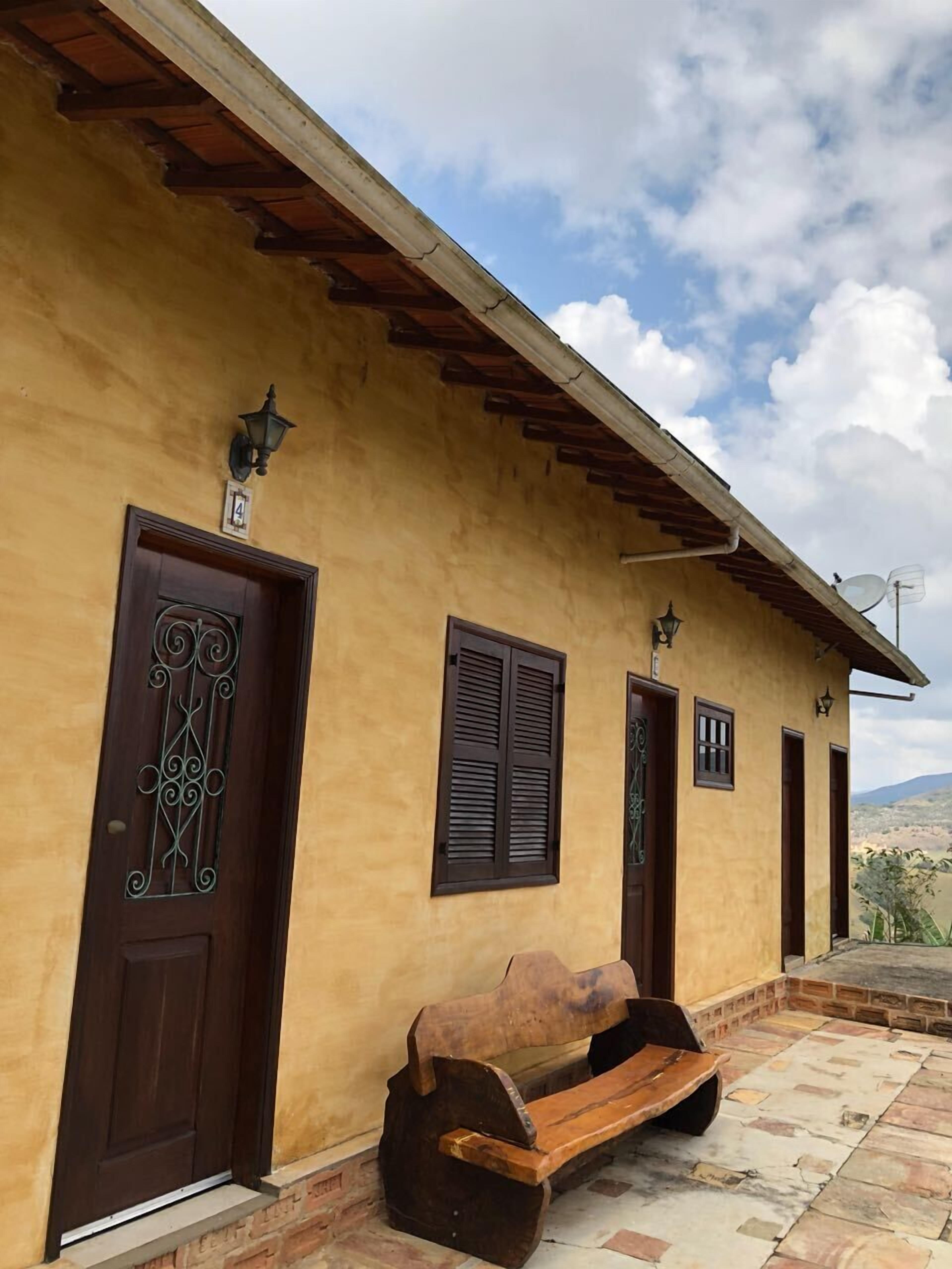 A building with a yellow facade, a wooden bench, and a door with a decorative metal design.