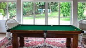 Una mesa de billar en una habitación con techo de madera y ventanas amplias.
