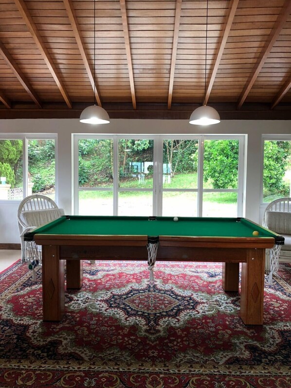 A pool table in a room with a wooden ceiling and large windows. - Pousada Lambari Montanha Hotel (Lambari)