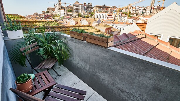 A rooftop terrace with potted plants, wooden benches, and a view of a cityscape with historic buildings and construction cranes. - Maria da Sé Historic House (Porto)