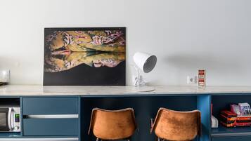 A kitchen counter with a large abstract painting, a white lamp, and two brown chairs.