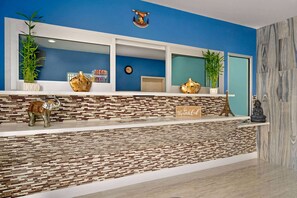 Un mostrador de recepción con una pared azul, un reloj y elementos decorativos, incluyendo una estatua de Buda y una planta.