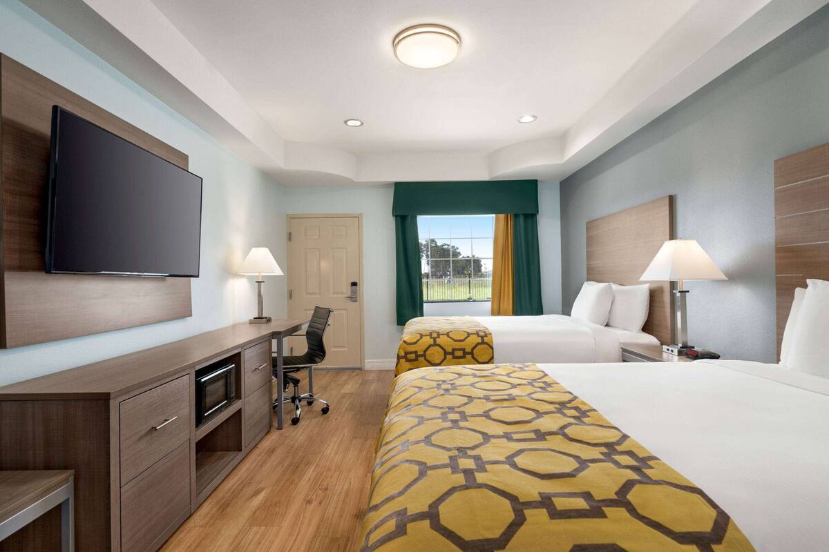 Hotelkamer met flatscreen-tv, bureau met stoel, twee bedden met beddengoed met dessin, en raam met gordijnen.