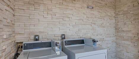 A laundry area with two commercial washers and dryers against a brick wall.