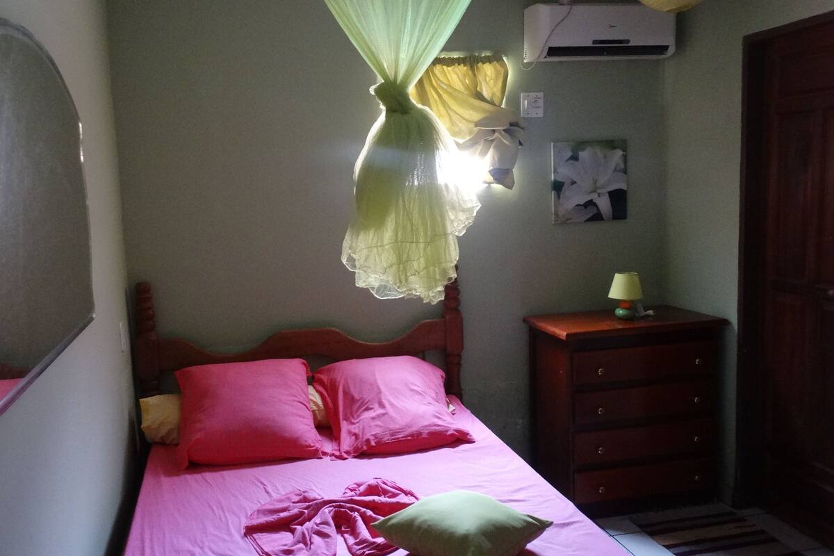 A bedroom with a bed, a nightstand, a dresser, a mirror, and an air conditioning unit.