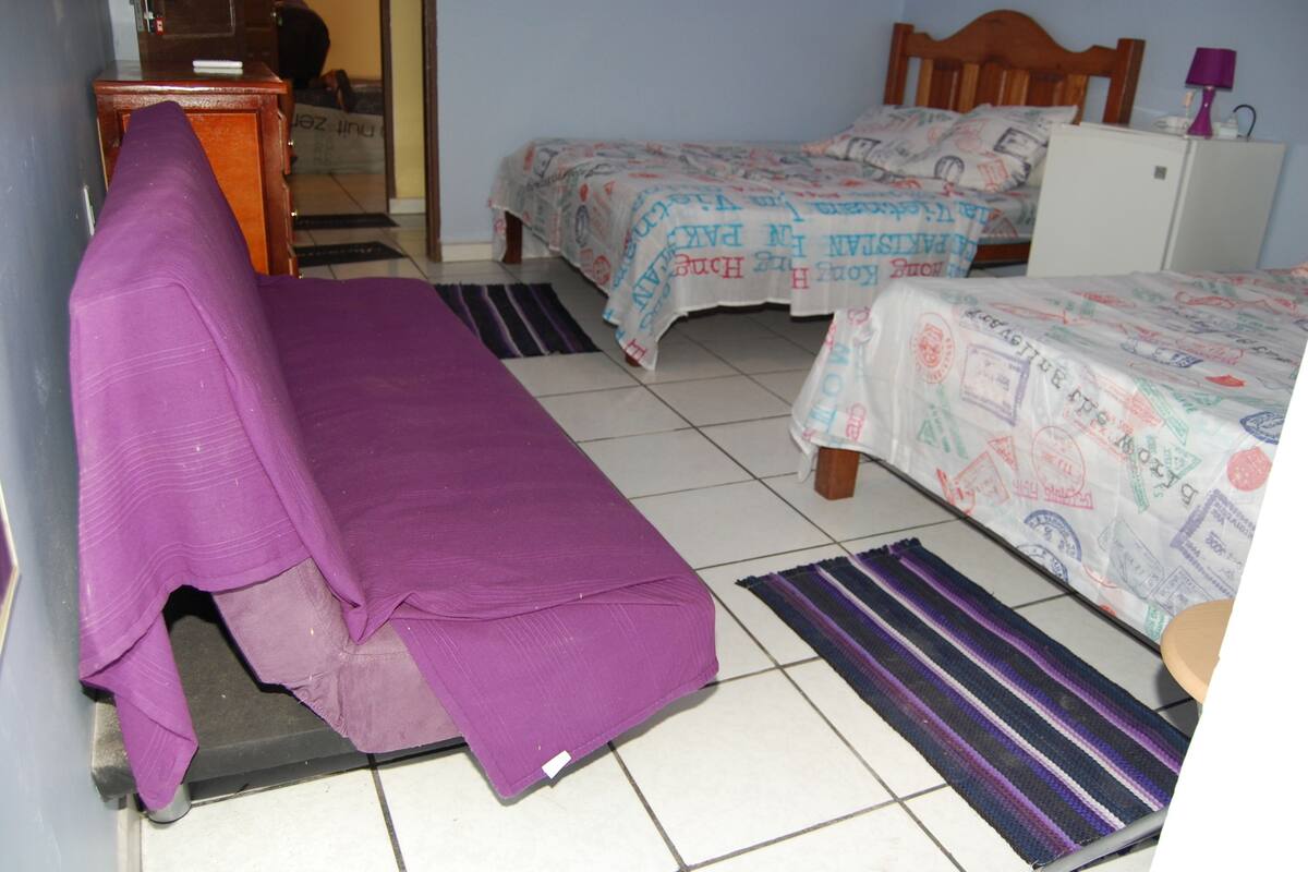 A room with two beds, a small desk, and a refrigerator.