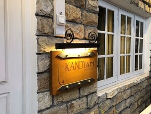 Een houten bordje met de tekst 'KANDYAPI COTTAGE' bevestigd aan een stenen muur.
