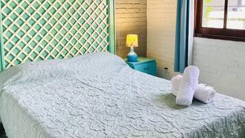 A bed with a patterned bedspread, a headboard with a lattice design, a nightstand with a lamp, and a window with curtains.