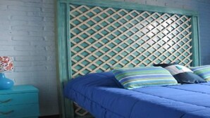 A bedroom with a blue bed, striped pillows, a blue nightstand, and a decorative wall panel. - El Viajero Hostels & Suites - Punta del Este (Punta del Este)