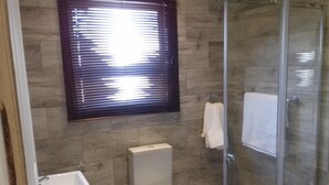 Un baño con cabina de ducha de vidrio, inodoro y lavamanos.