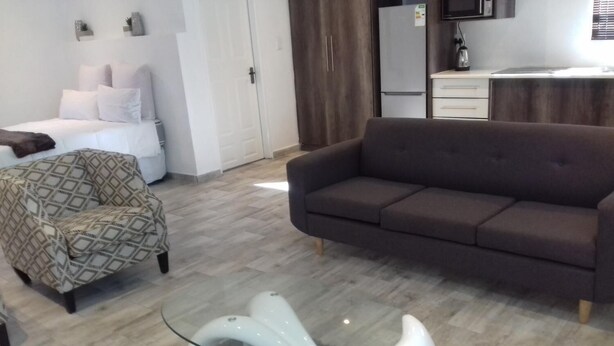 Una sala de estar moderna con un sofá marrón, un sillón estampado y una original mesa de centro de vidrio.