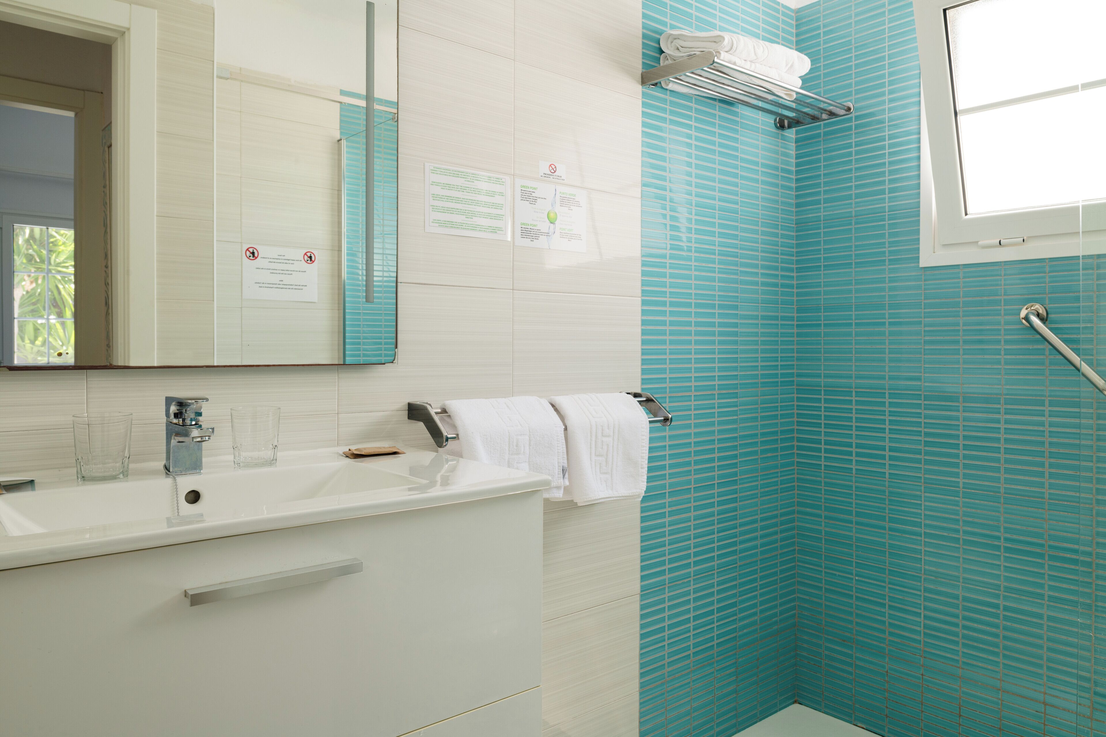 Ein Badezimmer mit einem weißen Waschbecken, einem Spiegel, einem Handtuchhalter und einem Fenster.