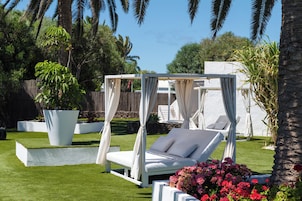 Un jardín con una cama con dosel blanco, una silla lounge blanca y una maceta grande con flores.