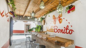 Zona de bar con mostrador de madera, dos taburetes, faroles colgantes y una pared con el letrero 'Valle Bonito'.