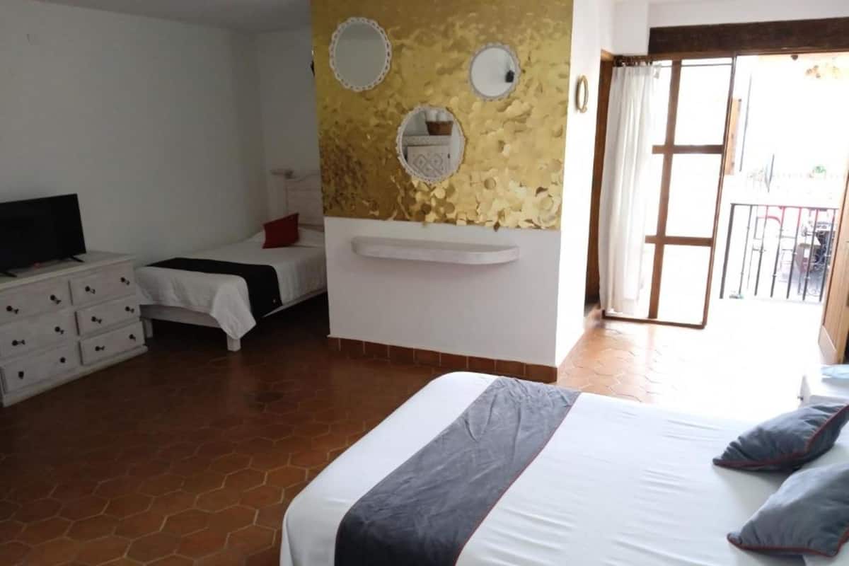 Un dormitorio con cama, cómoda, televisor y una pared decorada con placas.