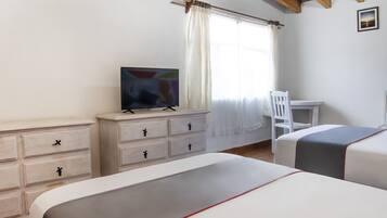 Un dormitorio con dos camas, un televisor sobre una cómoda, una silla y un escritorio.