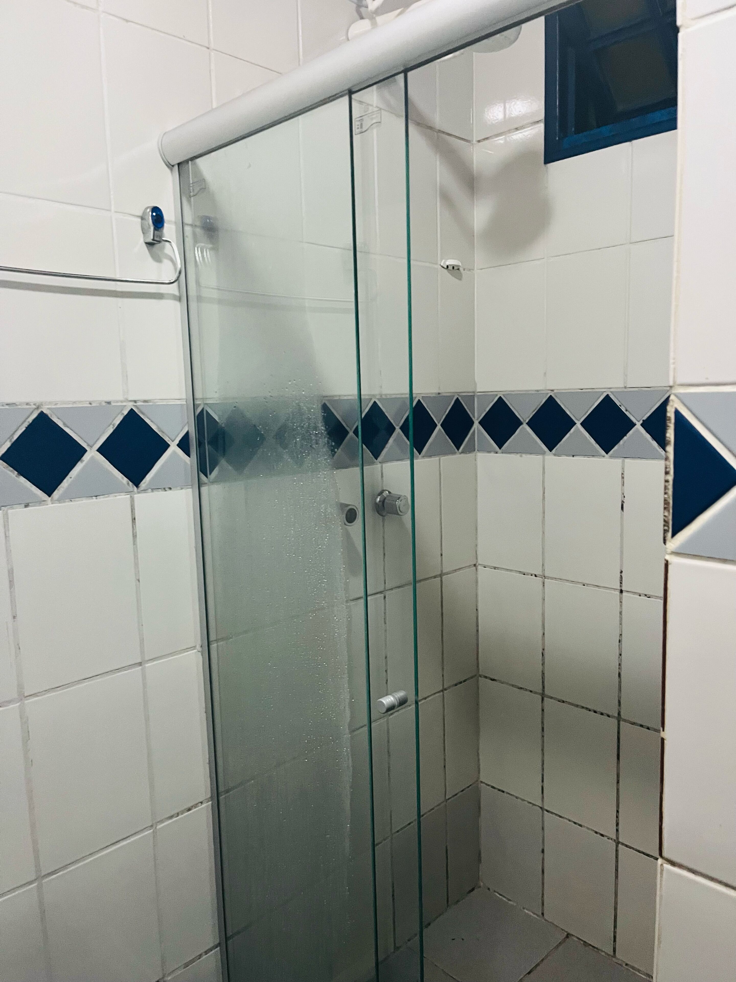 Cabina doccia con pareti piastrellate bianche e una bordura con motivo a rombi blu e bianchi.