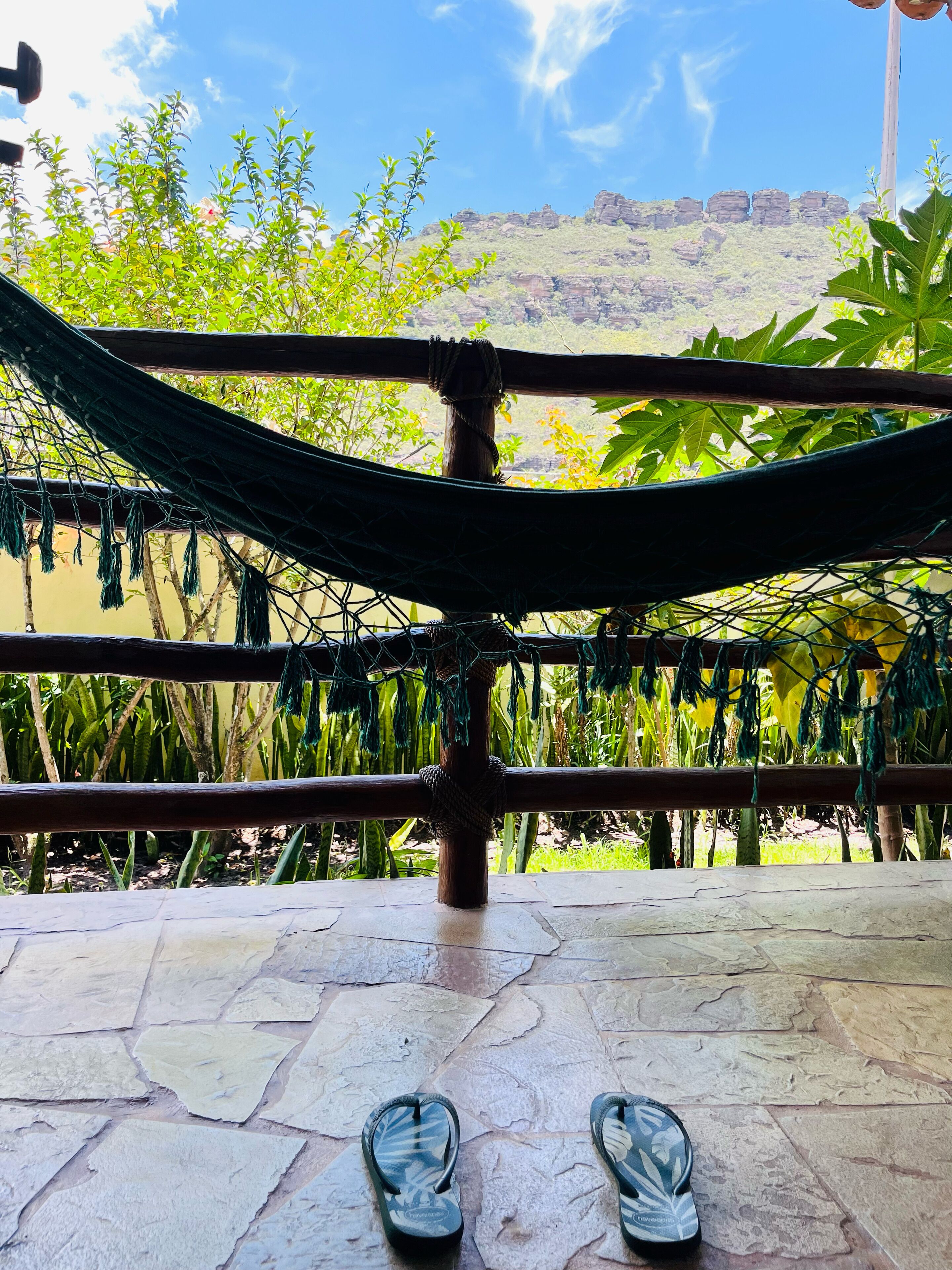 A hammock tied between wooden beams on a stone patio with a view of a mountainous landscape.