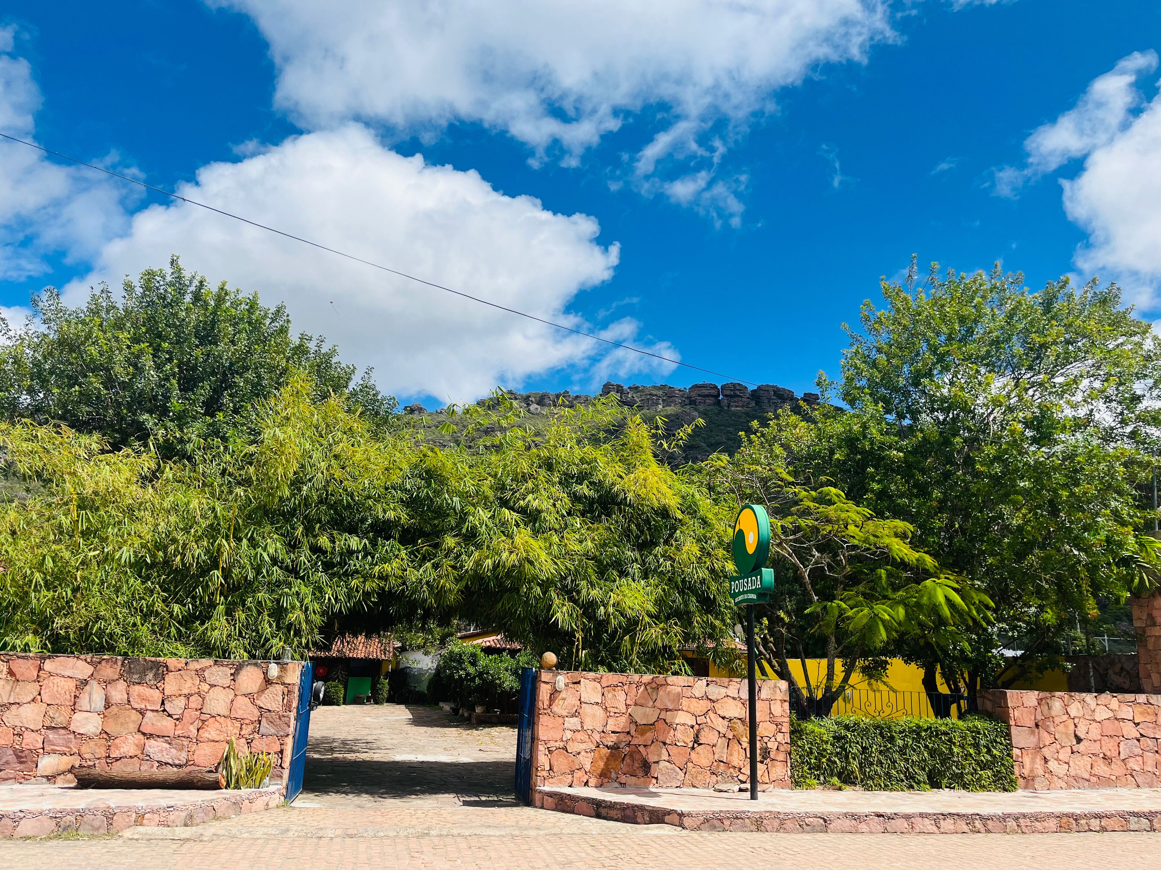 A stone-walled entrance with a green sign, lush greenery, and a mountain backdrop.