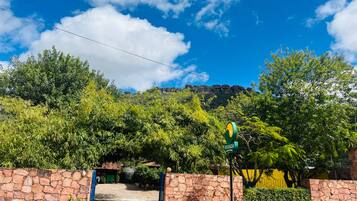 A stone-walled entrance with a green sign, lush greenery, and a mountain backdrop.