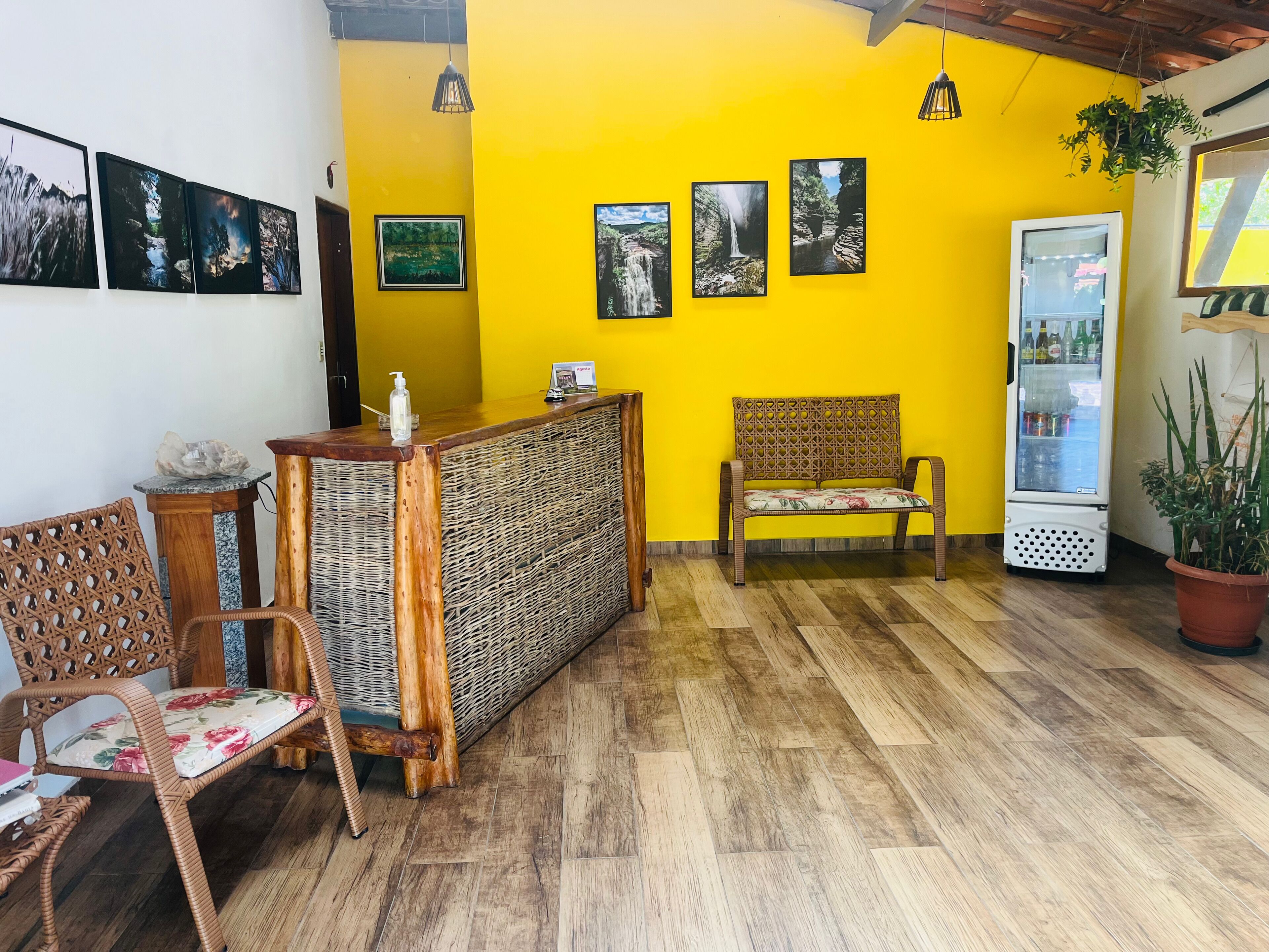 A reception area with a yellow wall, wooden reception desk, wicker chairs, and a refrigerator.