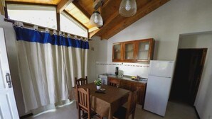 A compact kitchen with wooden cabinets, a dining table, and a refrigerator. - Cabañas Victoria (Mar de Las Pampas)