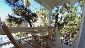 A wooden table and chairs on a balcony with a view of pine trees. - Cabañas Victoria (Mar de Las Pampas)