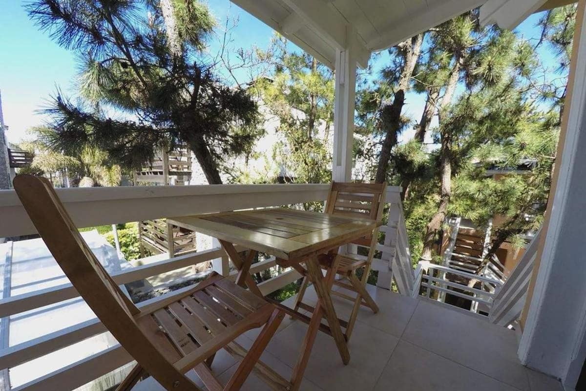 A wooden table and chairs on a balcony with a view of pine trees.