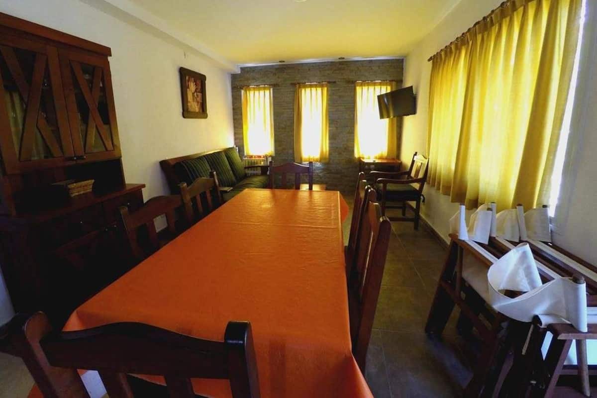 A dining room with a long table and chairs, a sofa, a television, and curtains.