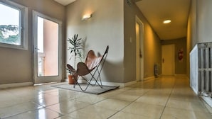 A spacious hallway with a tiled floor, a potted plant, a folding chair, and a radiator. - Trip Bariloche Select Hostel (San Carlos de Bariloche)