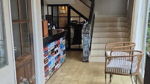 A spacious living area with a grey sofa, a wicker chair, a staircase, and a collection of colorful boxes on the floor. - Trip Bariloche Select Hostel (San Carlos de Bariloche)