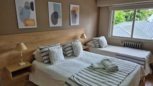 A hotel room with two beds, a wooden headboard, a nightstand, a lamp, and abstract wall art. - Trip Bariloche Select Hostel (San Carlos de Bariloche)