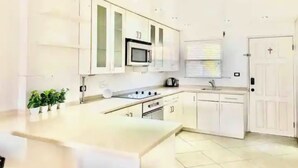 A modern kitchen with white cabinets, a central island, a microwave, and a stove. - Villa Marietta (Jolly Harbour)
