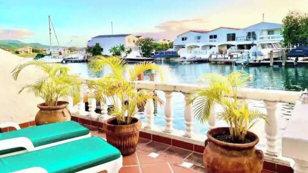 A terrace with potted plants, a railing, and a view of a marina with boats. - Villa Marietta (Jolly Harbour)