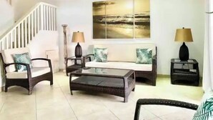 A spacious living room with a high ceiling fan, a staircase, a large painting, and two side tables with lamps. - Villa Marietta (Jolly Harbour)