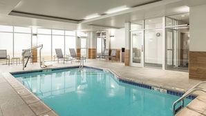 An indoor swimming pool with clear glass walls, a tiled floor, and a few lounge chairs.