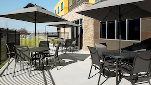 An outdoor patio area with tables and chairs, large umbrellas, and a stone building in the background.