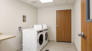 Un cuarto de lavandería con lavadora y secadora de carga frontal, una puerta de madera y un estante pequeño con dispensador de toallas.