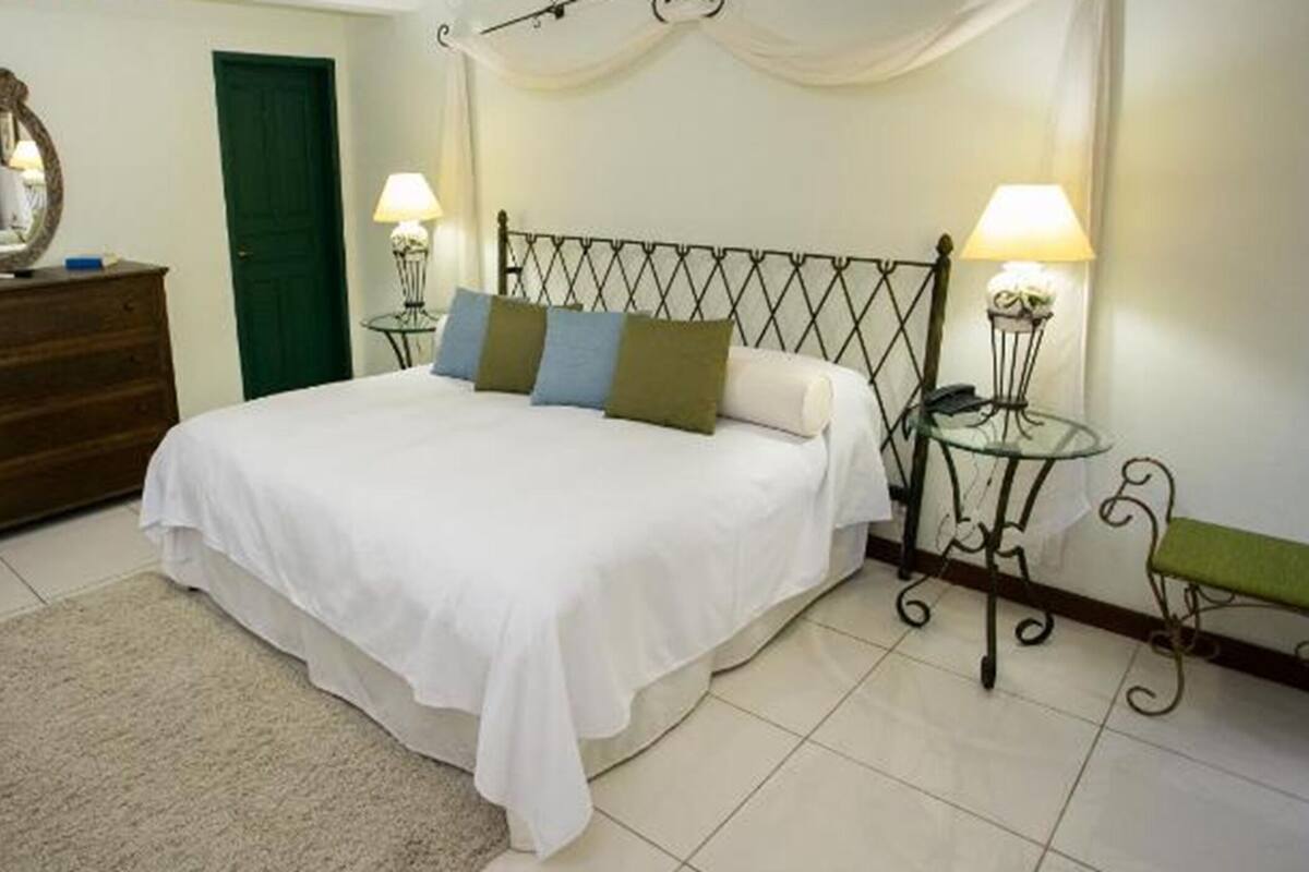Un dormitorio con cama, lámparas de noche, cómoda, espejo y una puerta verde.
